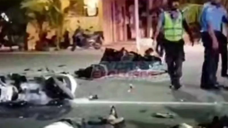 Night scene of a road accident on a street, with motorcycles and debris on the road, people lying on the ground and police officers in high-visibility vests standing nearby