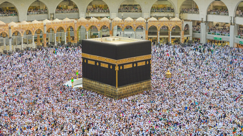 Thousands of pilgrims in white surround the black-draped Kaaba in the courtyard of Masjid al-Haram in Mecca during Hajj.