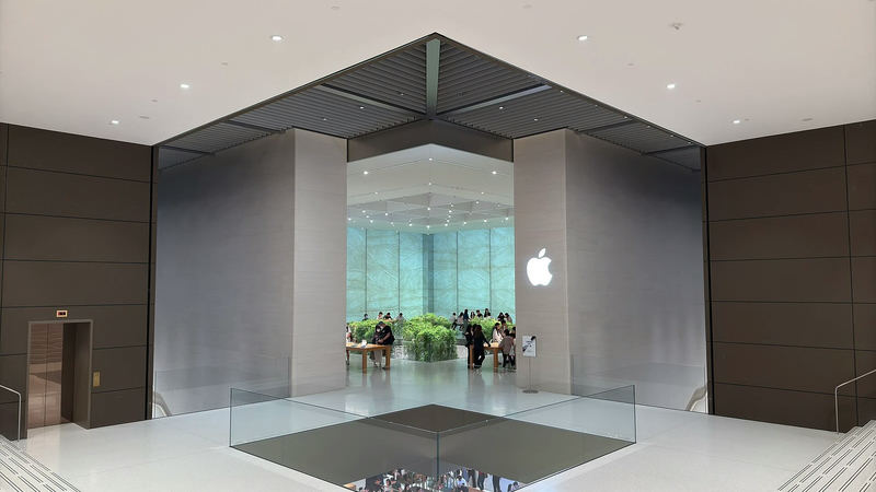 The entrance to an Apple Store at The Londoner Macao, with a large Apple logo on a glass wall and shoppers inside.