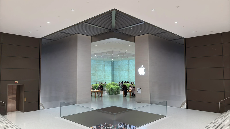 The entrance to an Apple Store at The Londoner Macao, with a large Apple logo on a glass wall and shoppers inside.