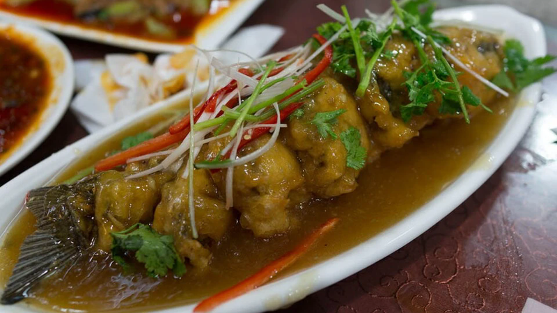 A whole fried fish in a red sweet and sour sauce on a plate.
