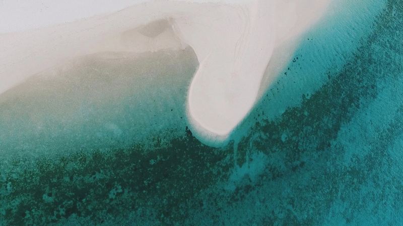 Aerial view of a white sandbank curving through a turquoise lagoon near Fenfushi