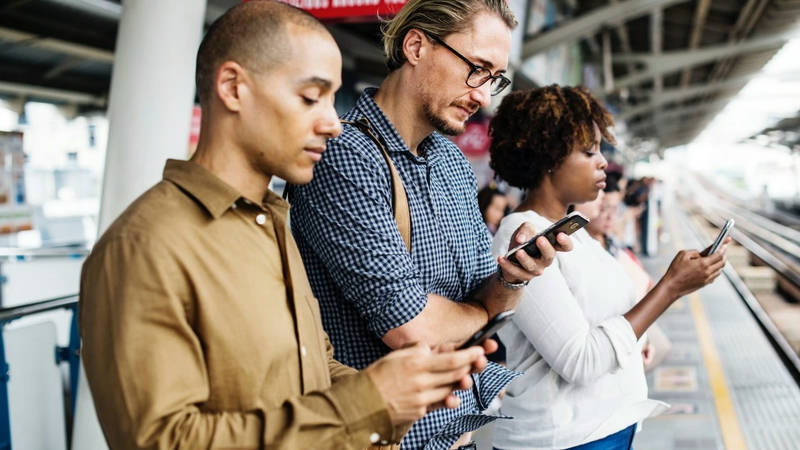People using smartphones on a railway station platform