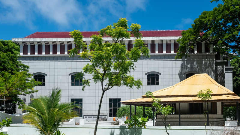 A whitewashed building with a red roof beside a yellow-roofed pavilion and a lawn in Malé