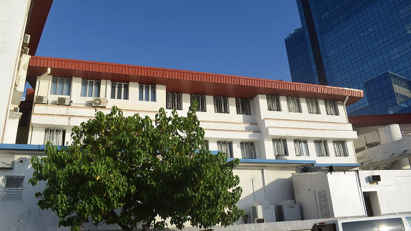 The Indira Gandhi Memorial Hospital building in Malé, seen from the street with a tree in front and a glass tower behind.