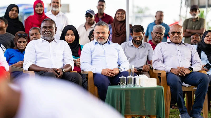 Minister Ahmed Shiyam seated in a light-blue shirt among officials and residents at an outdoor event in Addu Meedhoo