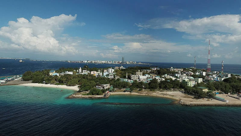 Aerial panorama of Villimalé island with its harbour, beach and telecom masts, Malé in the distance