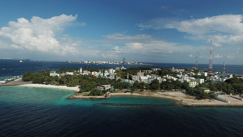 Aerial panorama of Villimalé island with its harbour, beach and telecom masts, Malé in the distance