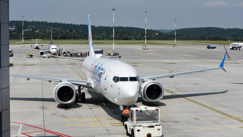 A white flydubai Boeing 737 parked on an airport apron, seen from the front with a tug positioned in front of it