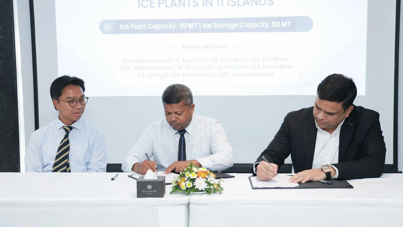 Three officials seated at a table signing an agreement, in front of a screen reading "Signing ceremony for the establishment of ice plants in 11 islands" and listing the islands.