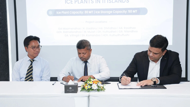 Three officials seated at a table signing an agreement, in front of a screen reading "Signing ceremony for the establishment of ice plants in 11 islands" and listing the islands.