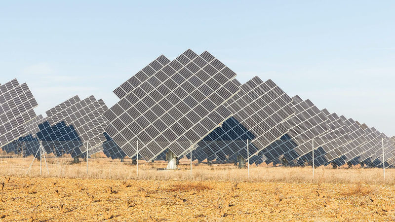 Large tilted solar panel arrays standing in a dry field under a clear blue sky