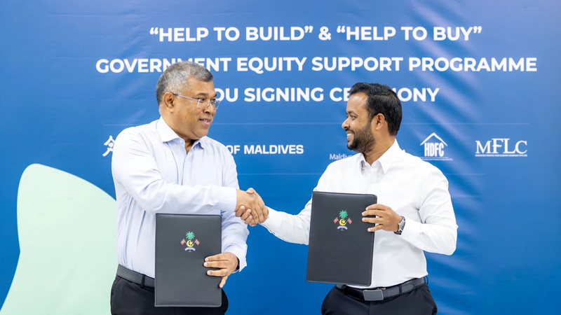 Two officials shake hands holding signed agreements in front of a Help to Build and Help to Buy banner