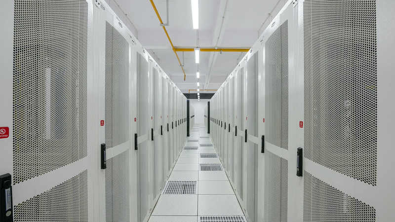 A long aisle between two rows of white server racks in a brightly lit data centre