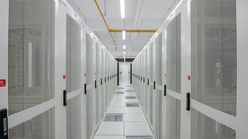 A long aisle between two rows of white server racks in a brightly lit data centre