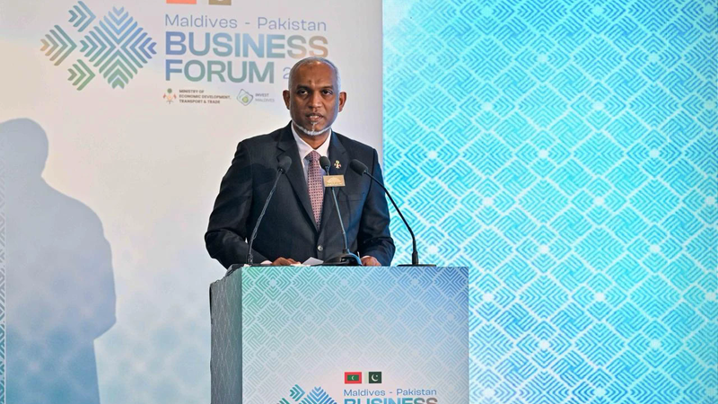 President Muizzu in a dark suit speaking at a lectern in front of a Maldives–Pakistan Business Forum 2026 backdrop
