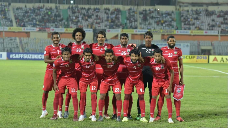 Maldives football players in red kits posing for a team photo on a stadium pitch