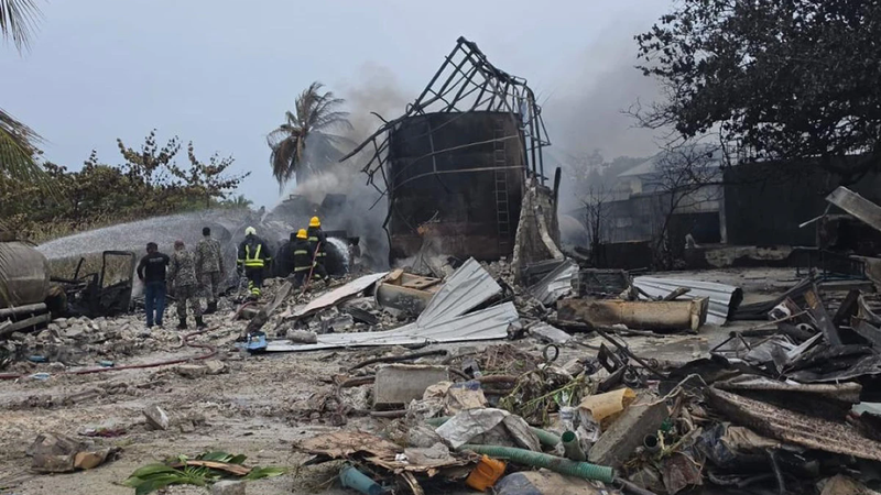 Firefighters spray water near a burnt-out fuel tank amid debris and smoke after a fire in Funadhoo, Maldives