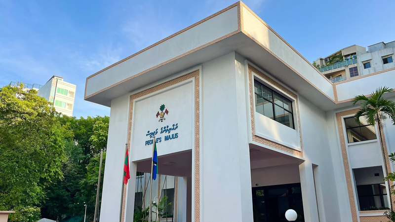 White People's Majlis building with the Maldives emblem and flags at its entrance under a blue sky