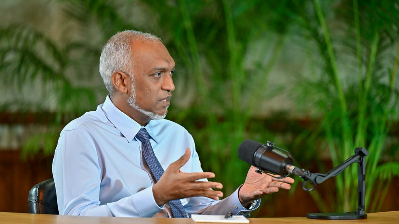 President Mohamed Muizzu speaks into a microphone at a wooden desk while discussing the 2027 budget on a podcast