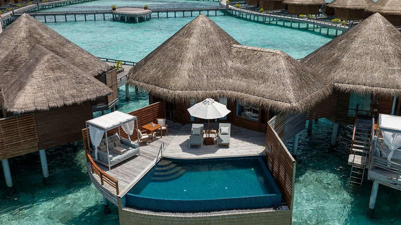 Aerial view of thatched overwater villas with a private pool and deck above a turquoise lagoon at Baros Maldives