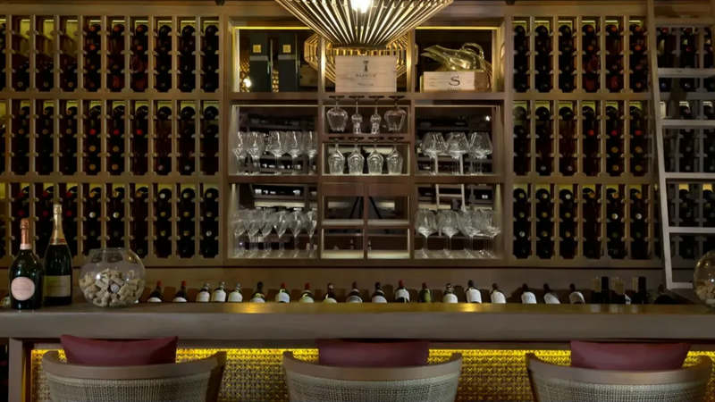 Wine cellar with wooden racks of bottles, glassware shelves and a lit tasting counter with three chairs at Vakkaru Reserve, Vakkaru Maldives